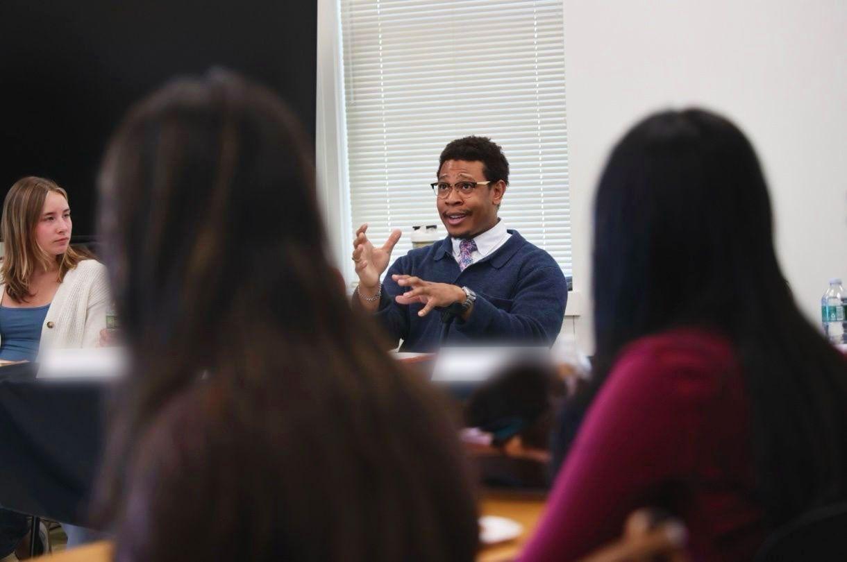 Quson G. Brown speaking, mid-gesture, across a seminar table at the Cornell Brooks School.