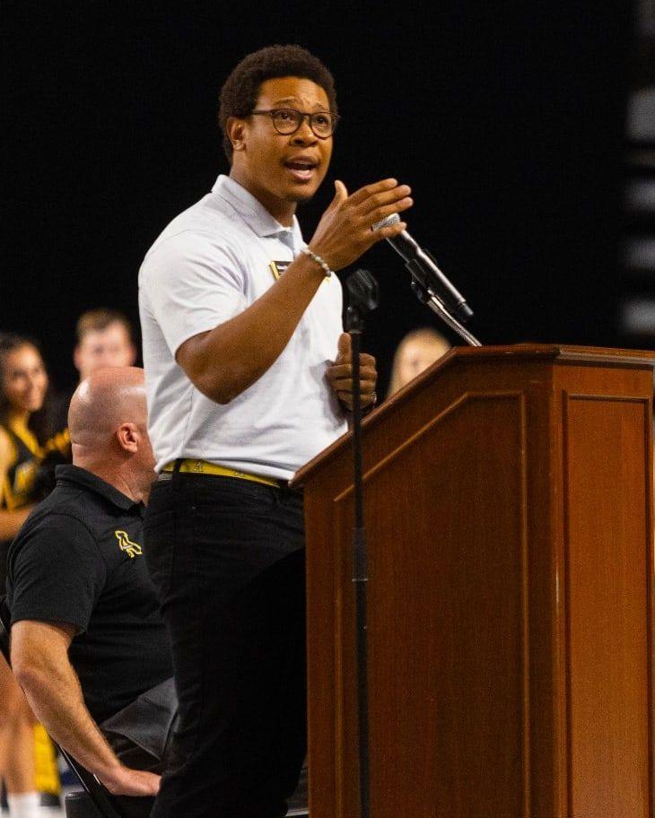 Quson G. Brown addressing an arena from a wooden lectern at Appalachian State University.
